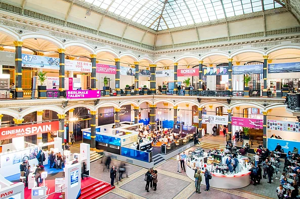 Große helle Messehalle mit Glasdach und mehreren Ausstellungsständen sowie Besuchern auf zwei Ebenen