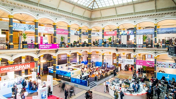 Große helle Messehalle mit Glasdach und mehreren Ausstellungsständen sowie Besuchern auf zwei Ebenen