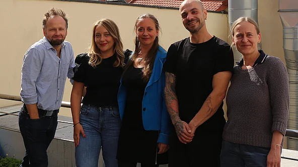Fünf Personen stehen nebeneinander vor einer hellen Wand, drei Frauen und zwei Männer, alle lächelnd 