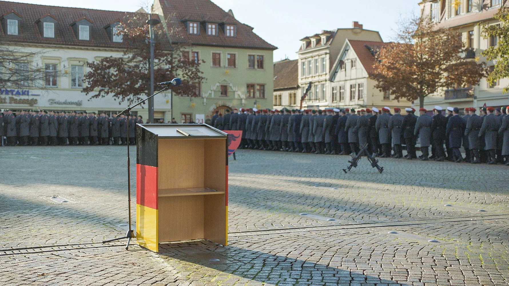 Dorfplatz mit leerem Rednerpult, im Hintergrund Soldaten der Bundesweh