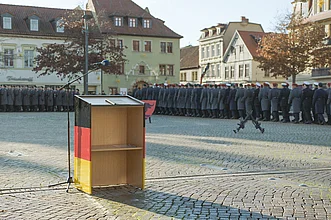 Dorfplatz mit leerem Rednerpult, im Hintergrund Soldaten der Bundesweh