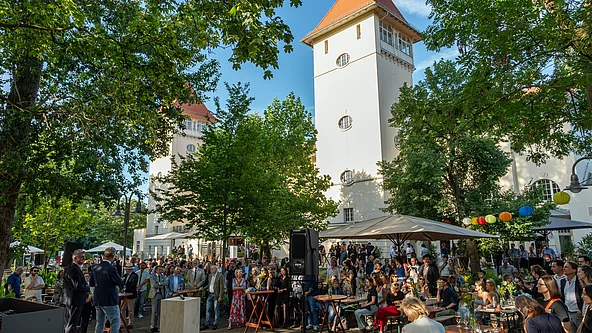Große Menschenmenge bei einer Veranstaltung im Freien vor einem historischen Gebäude mit zwei Türmen und roten Dächern