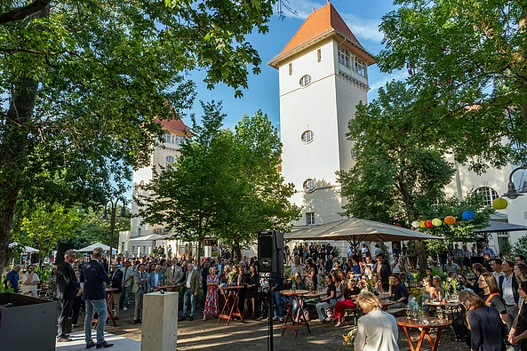Große Menschenmenge bei einer Veranstaltung im Freien vor einem historischen Gebäude mit zwei Türmen und roten Dächern
