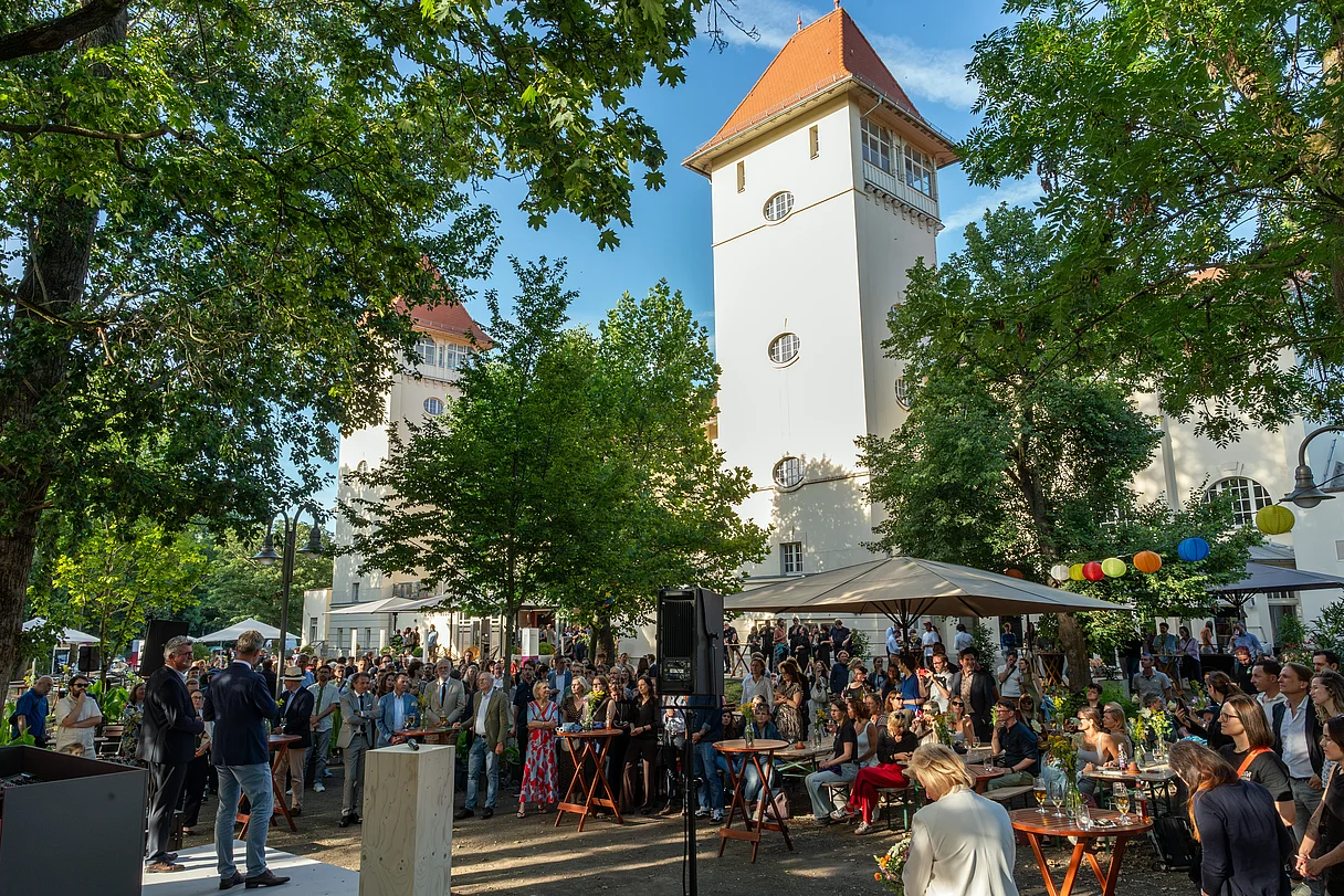 MDM Sommerfest 2026 Große Menschenmenge bei einer Veranstaltung im Freien vor einem historischen Gebäude mit zwei Türmen und roten Dächern