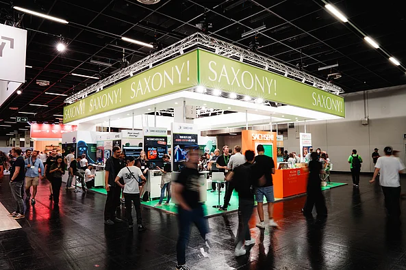 Messestand mit grünem Banner und der Aufschrift »SAXONY!« auf einer Messe mit vielen Besucher*innen