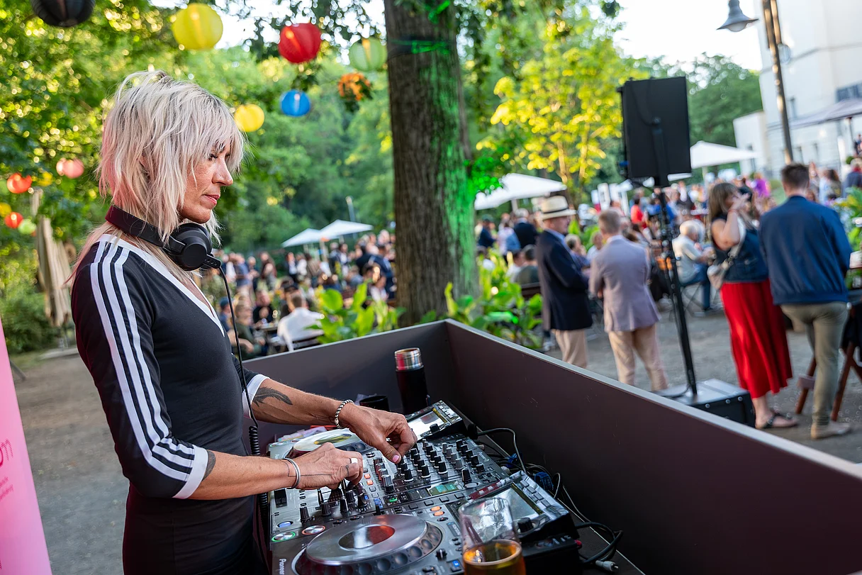 MDM Sommerfest 2026 DJ mit Kopfhörern bedient Mischpult auf einer Sommerveranstaltung im Freien mit Gästen im Hintergrund