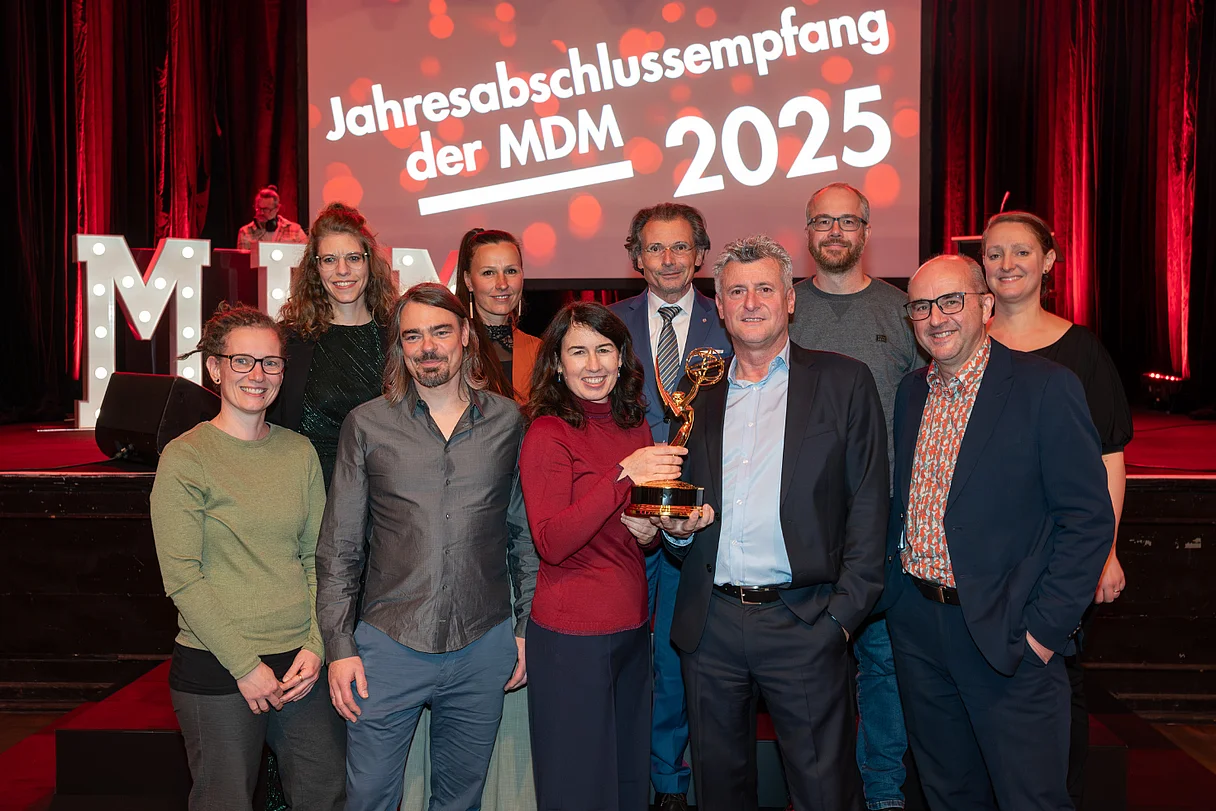 MDM Jahresabschlussempfang 2025 Großes Gruppenfoto mit vielen Teilnehmenden auf einer Bühne, im Hintergrund die Leinwand „Jahresabschlussempfang der MDM 2025“.