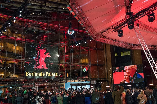 Berlinale Menschenmenge vor dem beleuchteten Berlinale Palast am Potsdamer Platz in Berlin; über dem Eingang das rote Bärenlogo und eine große Videoleinwand.