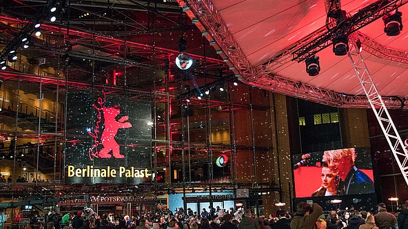 Berlinale Menschenmenge vor dem beleuchteten Berlinale Palast am Potsdamer Platz in Berlin; über dem Eingang das rote Bärenlogo und eine große Videoleinwand.