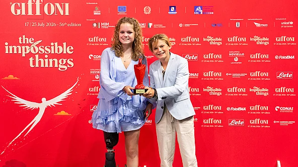 Zwei Jugendliche vor rotem Hintergrund mit Schriftzug "Giffoni" und "the impossible things" halten gemeinsam eine rote Trophäe